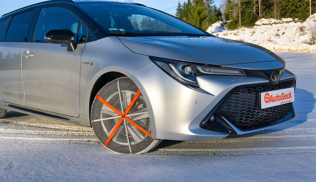 AutoSock tire socks mounted on front wheels of a grey Toyota Corolla car, standing on snow
