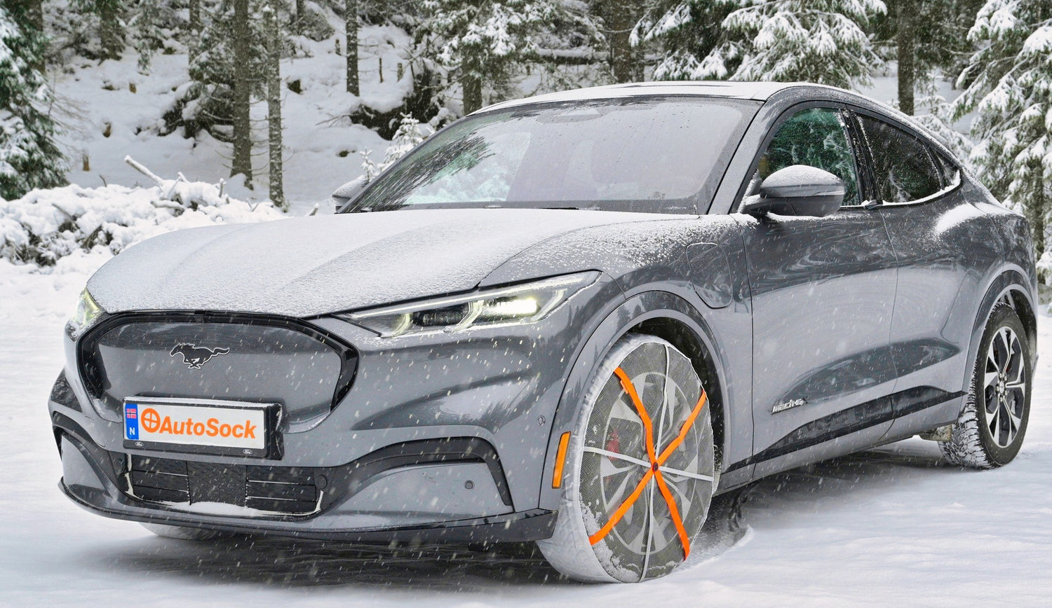 AutoSock mounted on front wheels of grey Ford Mustang passenger car, standing on snow