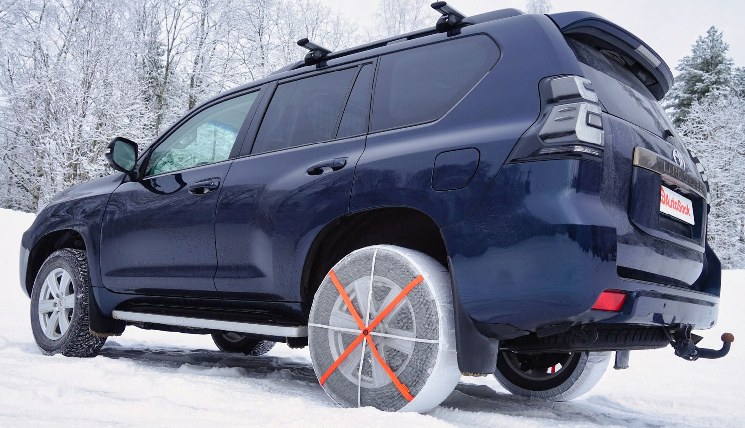 Toyota Land Cruiser off-road vehicle SUV with textile snow chains mounted on rear wheels, standing on snow