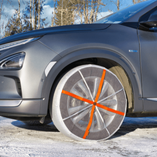 AutoSock textile snow chains mounted on front wheels of a passenger car, standing on snow in woods